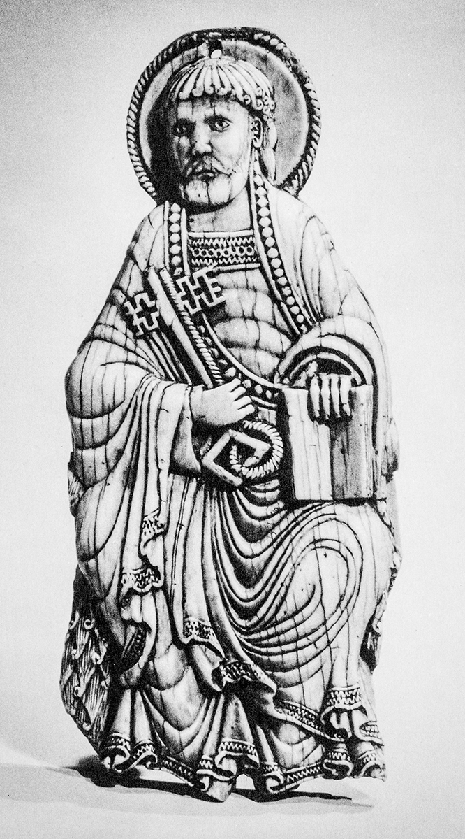 An ivory plaque depicting a seated man wearing robes and a halo, holding two large keys in his right hand and an open book in his left hand.