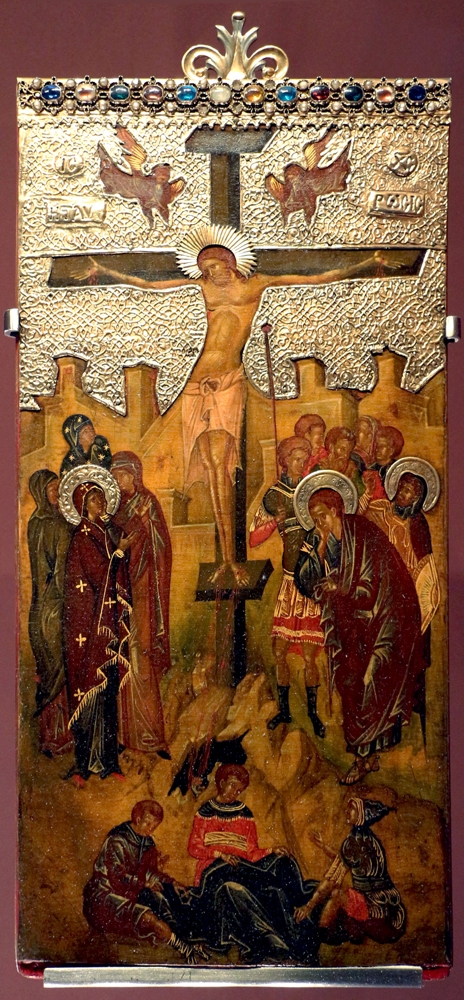 On the painted cover of a reliquary with some metalwork, a man on a cross surrounded by other figures in a landscape with buildings in the background.