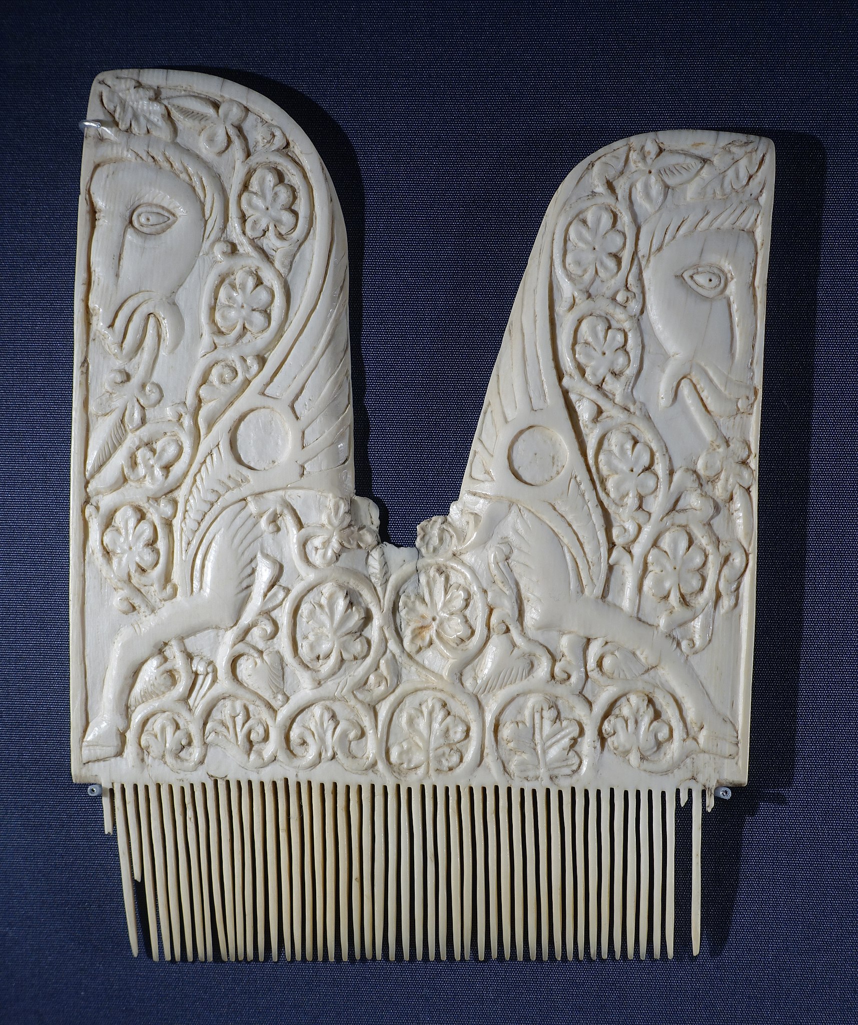 An ivory comb with a lyre-shaped handle carved with two winged horses in vines.