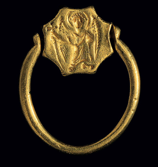 On the reverse of the rotating bezel of a gold ring is a standing, winged figure holding a cross.