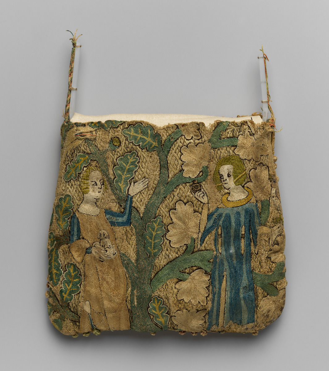 Squarish textile purse of mainly gold, green, blue and white threads, depicting scene of courting lovers. Standing female figure raising hand and holding dog, before man raising ring in right hand, both flanking stylized leafy tree. Missing strap and some parts threadbare.