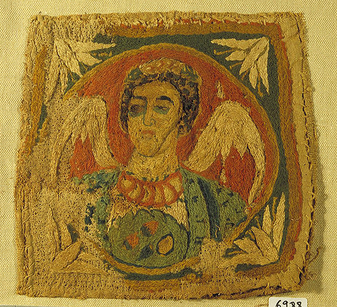 A square piece of fabric with a winged angel inside a circle, all within a square frame.
