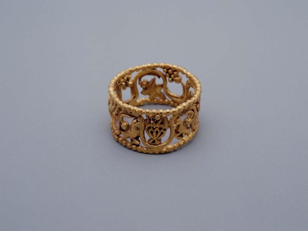 Within the openwork of a gold ring, a grapevine winds among a pair of birds flanking a vase.