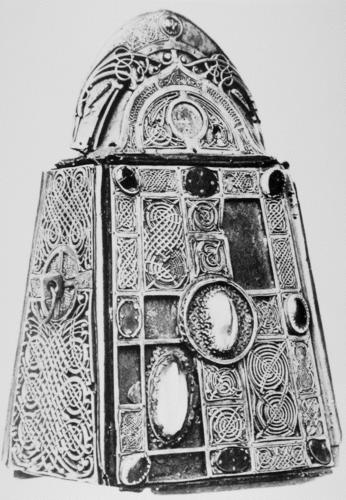 Black and white photograph of decorated metal bell case and reliquary, fit with oval rock crystals, gems, and silver and silver-gilt ornamental patterns of interlace.