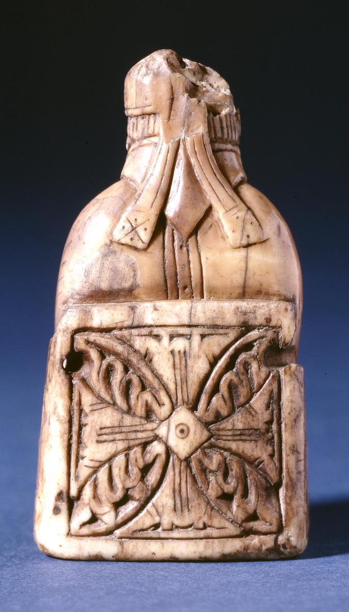 Carved ivory chess piece of bishop from reverse revealing the back of the miter and a chair decorated with four-petaled foliate ornament.