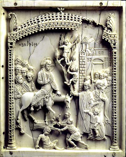 Carved rectangular ivory panel depicting a bearded man wearing a cross in halo and seated sideways on a saddled ass, followed by a group of bearded men, and the foreground two male figures are spreading a garment, and a youthful male seated on the ground looking at his foot. At the right, figures emerge from a city gate and two youthful figures climb a tree. The scene beneath an openwork canopy and Greek inscription in background.