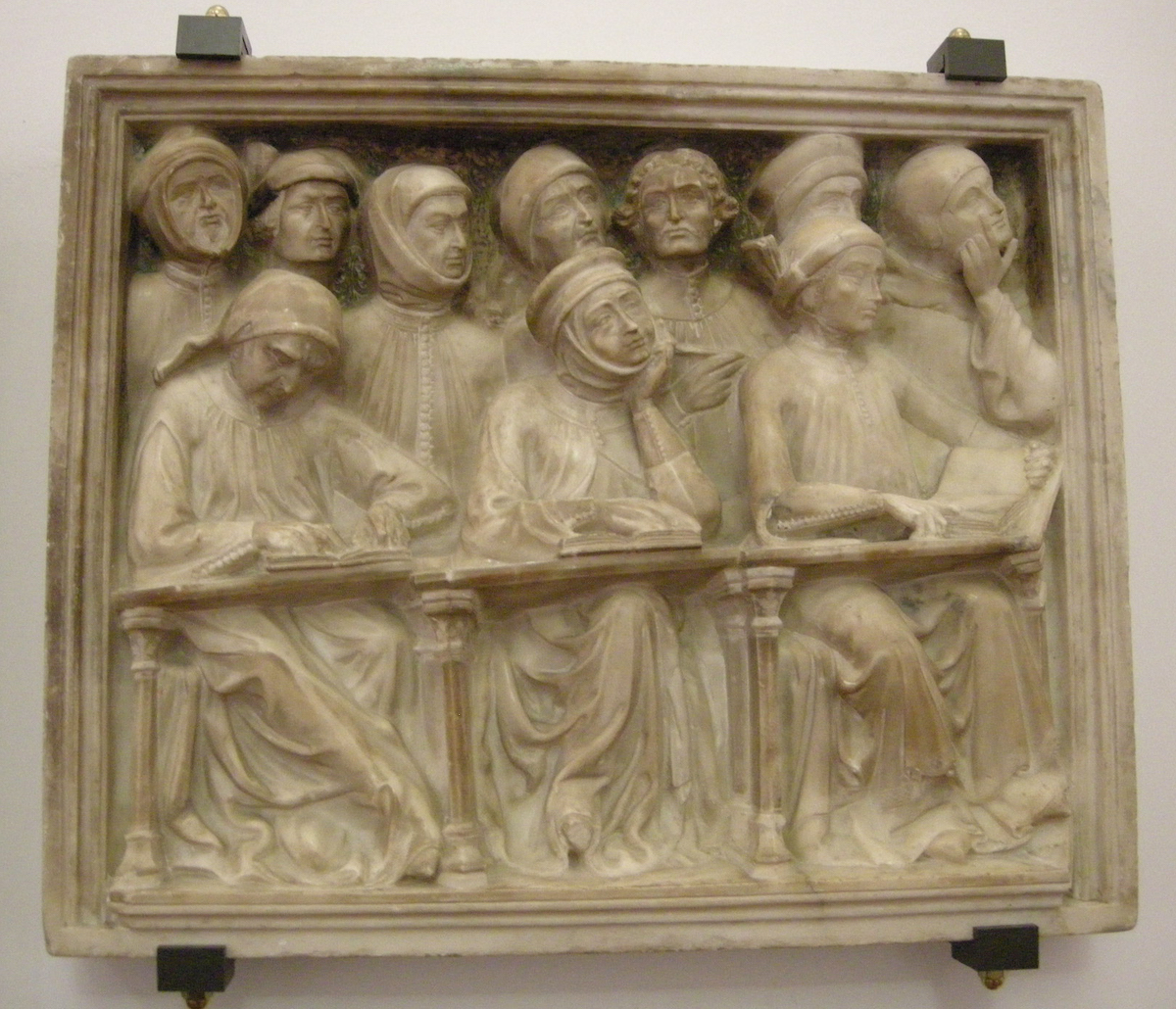 Rectangular stone panel carved with group of ten men, some wearing headgear and three in front of books on desks. Traces of polychromy and ruled frame.