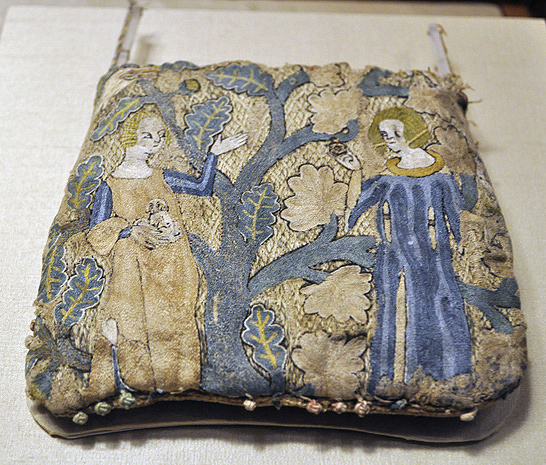 Squarish textile purse of mainly gold, green, blue and white threads, depicting scene of courting lovers. Standing female figure raising hand and holding dog, before man raising ring in right hand, both flanking stylized leafy tree. Missing strap and some parts threadbare.