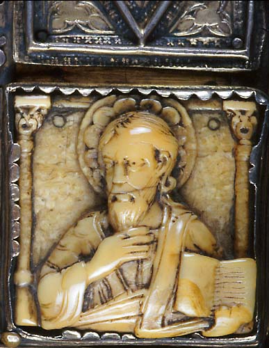 A walrus ivory plaque that contains a haloed bearded man raising his right hand and holding an open book in his left hand.