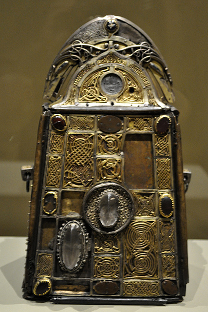 Decorated metal bell case and reliquary, fit with oval rock crystals, gems, and silver and silver-gilt ornamental patterns of interlace.