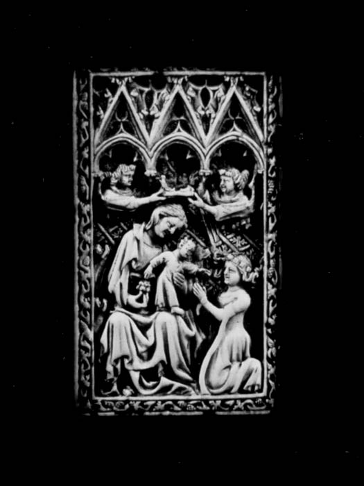 On a carved ivory panel, a figure kneeling before a child on a woman’s lap.