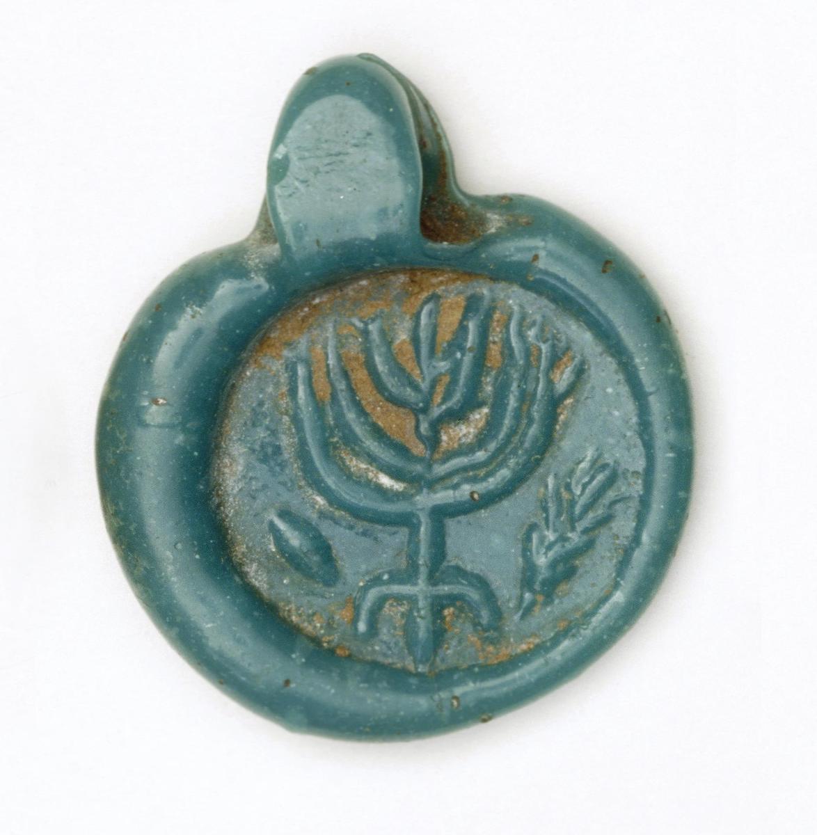 Round blue glass pendant decorated with a seven-branched candelabra (menorah) flanked by a citron fruit (etrog) and a palm frond (lulav). Suspension loop at top.