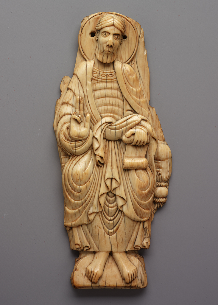 An ivory plaque depicting a seated man wearing robes and a halo, his right hand raised and his left hand holding a scroll.