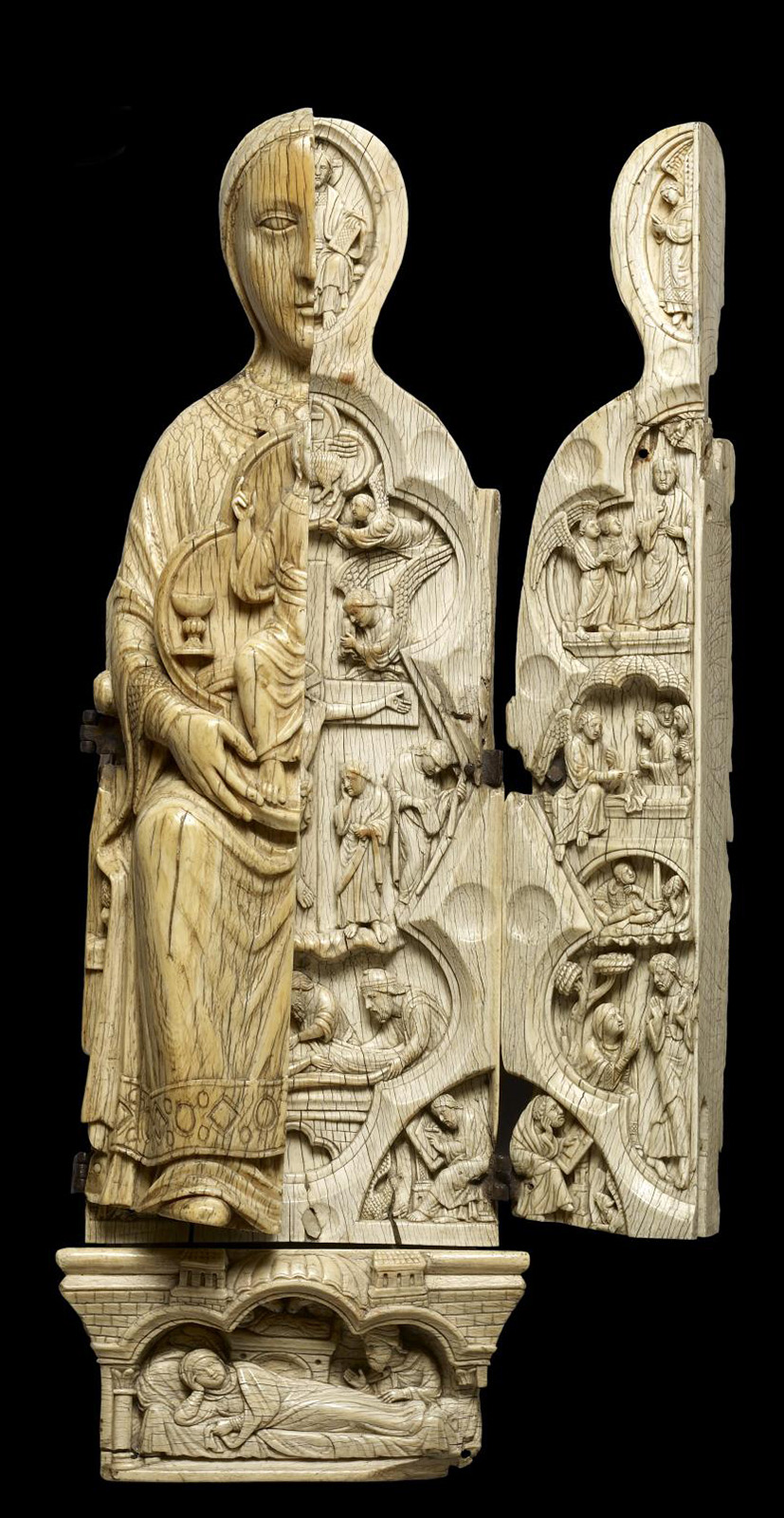 An ivory triptych in the form of a seated woman, right wing open, carved with many figures in multiple scenes.