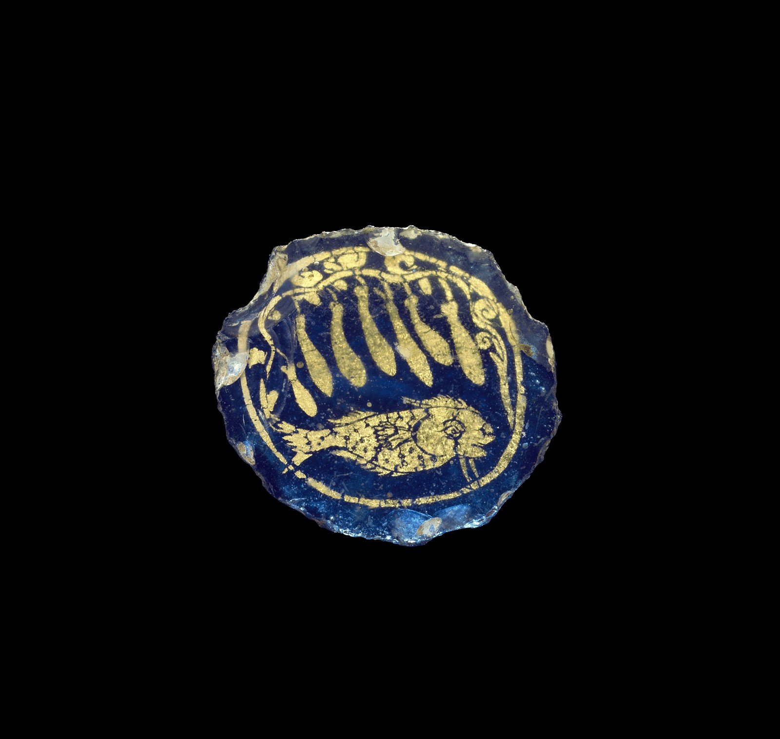 A blue gold glass medallion that contains a representation of a fish under a vine bearing multiple gourds.  