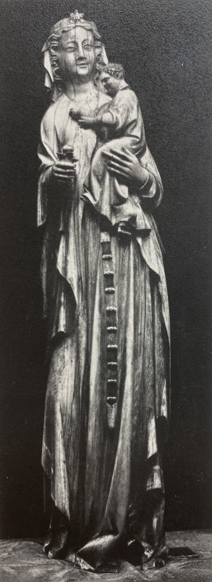 Carved ivory statuette of a veiled woman, wearing long belted garment, holding a male child in her left arm and bud of flower in her other hand.