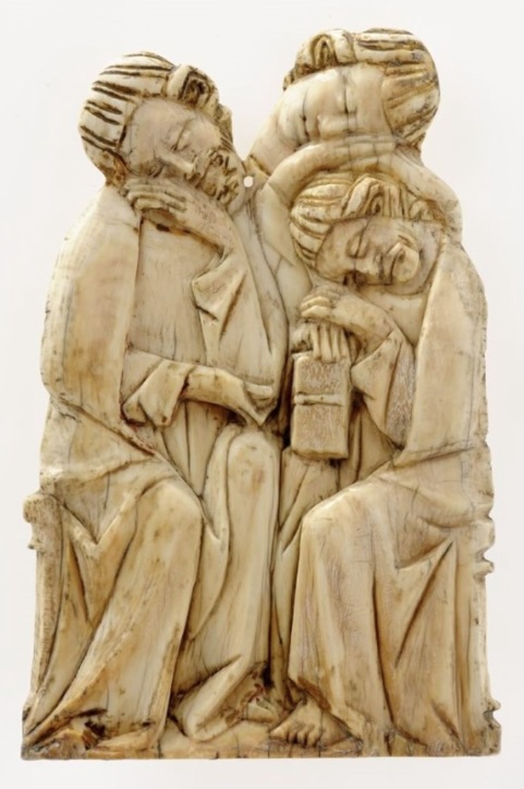A carved ivory relief fragment depicting three men, two bearded, eyes closed, leaning on their hands, one holding a closed book on their lap, all seated.