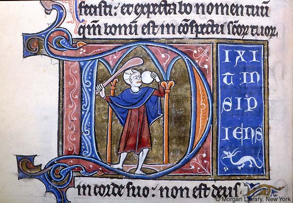Manuscript page detail of pink and blue initial D enclosing bald man raising club and round, white loaf between columns, gold background. At right, four lines of Latin text continue on blue block above line ending ornament of white dragon in profile.