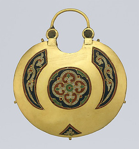 The back of a circular gold pendant, decorated with a four-leaf design in a circle and three curved abstract forms.