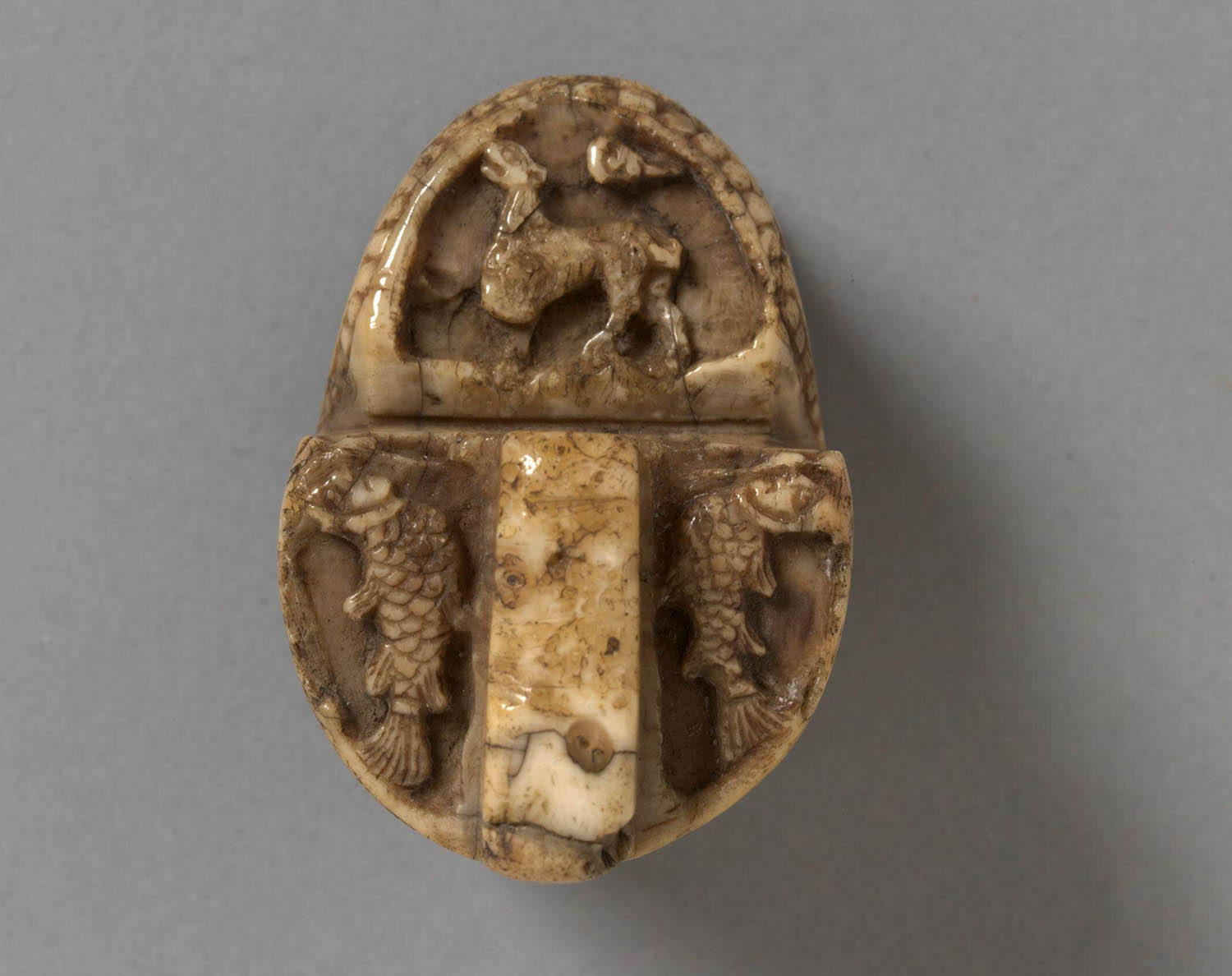Top of a chess piece decorated with human figures, animals, and ornament.